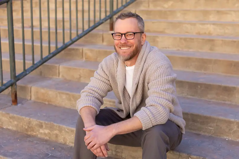 Patrick Maguire, smiling, seated on a flight of stone steps in late afternoon light